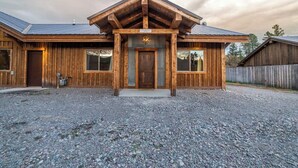 A rustic wooden building with a prominent front entrance, large windows, and a gravel driveway.