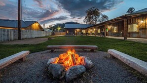 A rustic outdoor area with a fire pit, wooden benches, and a building with a metal roof.