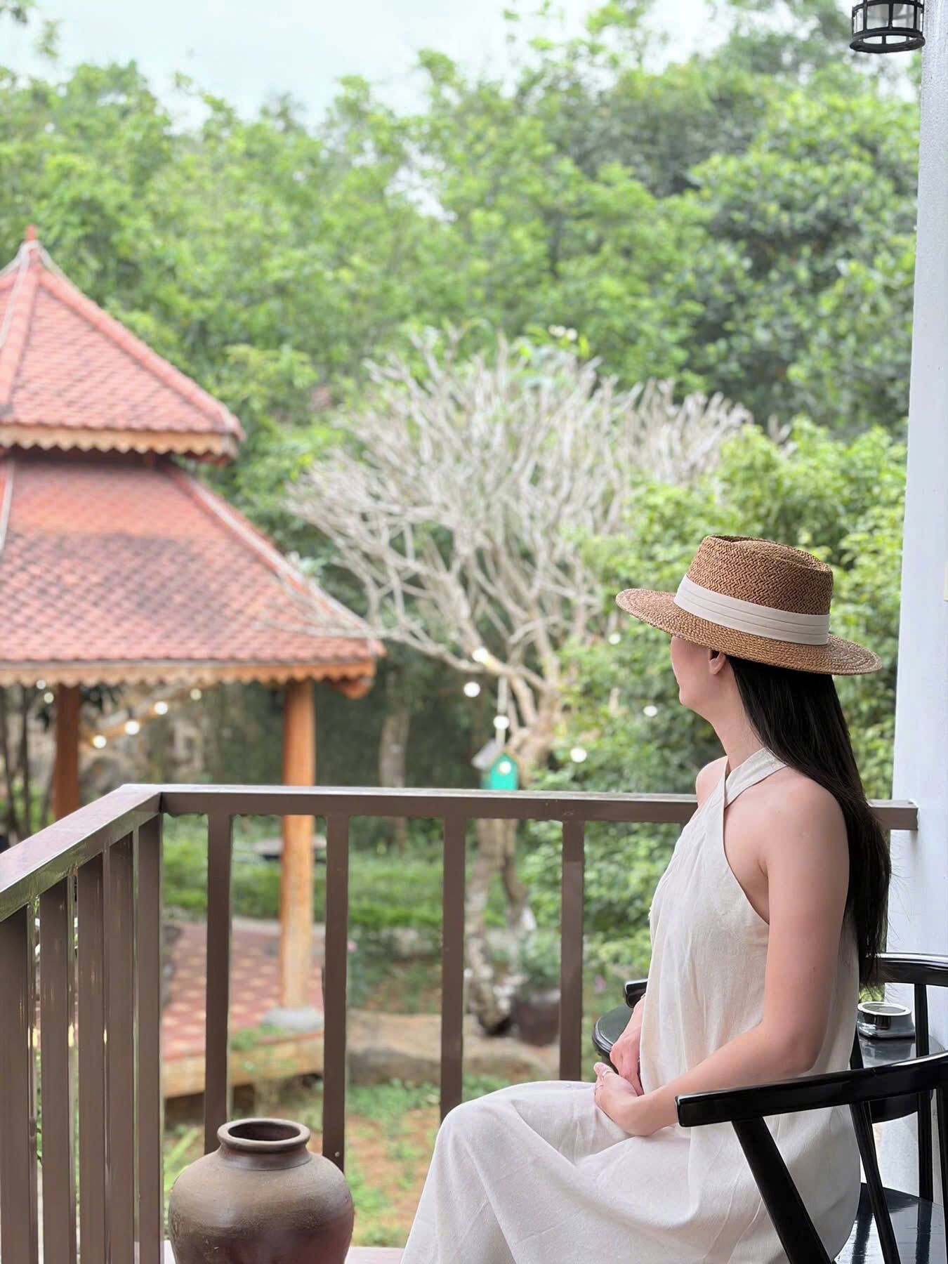 A person seated on a balcony with a view of a traditional building and lush greenery.