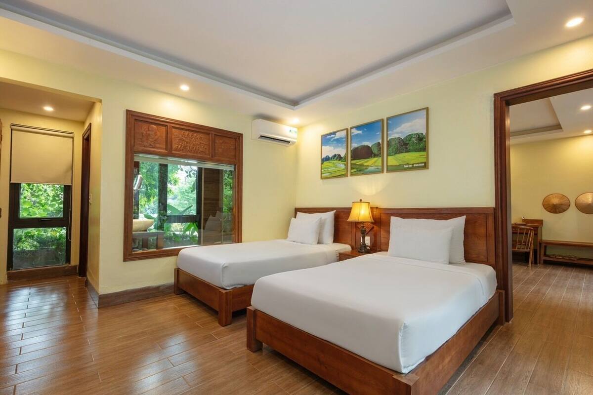 Quarto de hotel com duas camas, janela com vista para áreas verdes, um armário de madeira e um ar condicionado fixado na parede.