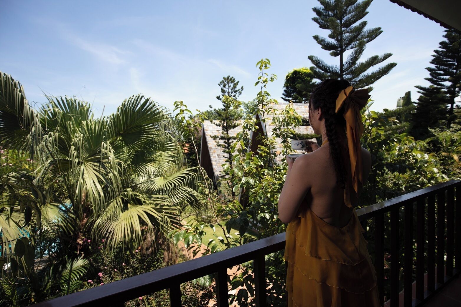 Eine Person steht auf einem Balkon mit Blick auf üppige tropische Vegetation und eine Steinmauer.