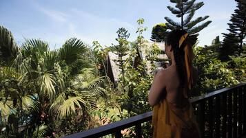 A person standing on a balcony with a view of tropical vegetation and a stone wall.