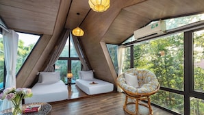 A room with a sloped ceiling, large windows, a bed, a chair, and a table with a book. - Bai Dinh Garden Resort & Spa Ninh Binh (Tay Hoa Lu)