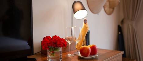 Un tavolo in legno con un vaso di fiori rossi, un bicchiere di vino, una bottiglia di champagne e un piatto con due mele.