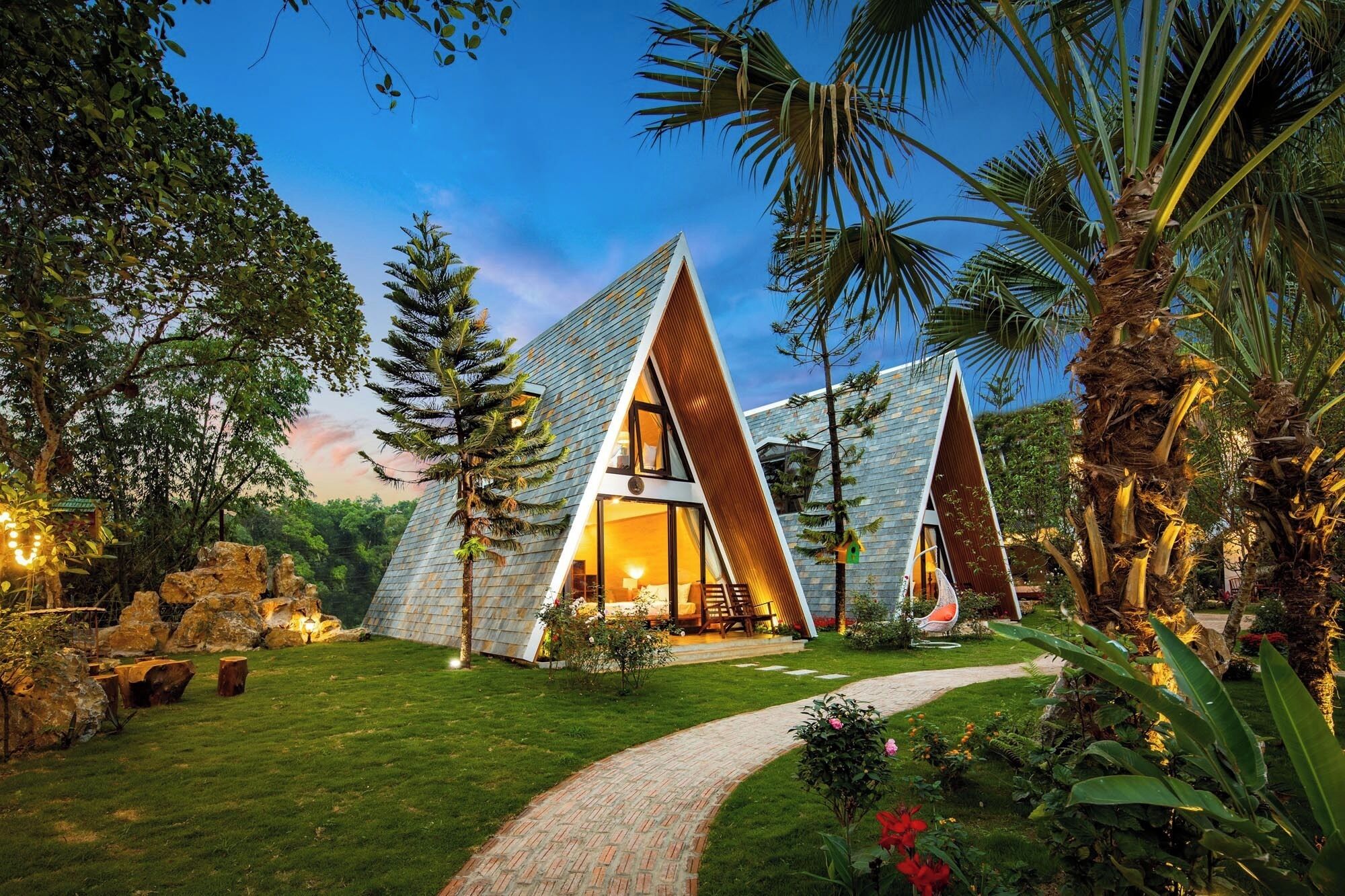Un edificio moderno dalla forma triangolare, con facciata in vetro, immerso nel verde e circondato da un giardino curato.