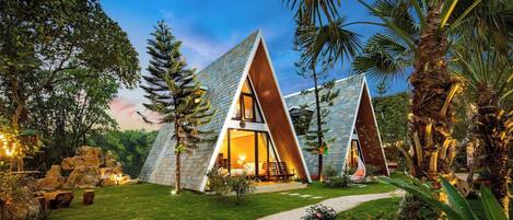 A modern, triangular-shaped building with a glass facade, surrounded by lush greenery and a well-maintained garden.