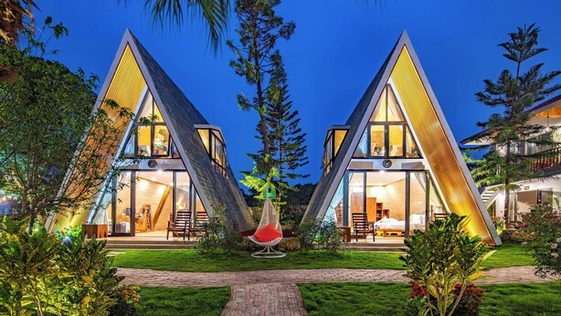 Two modern, triangular-shaped buildings with large windows, surrounded by lush greenery and palm trees. - Bai Dinh Garden Resort & Spa Ninh Binh (Tay Hoa Lu)