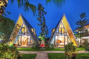 Dos edificios modernos de forma triangular con amplios ventanales, rodeados de exuberante vegetación y palmeras.