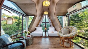 A modern, triangular room with a large window, two white beds, a wicker chair, and a small table with a vase. - Bai Dinh Garden Resort & Spa Ninh Binh (Tay Hoa Lu)