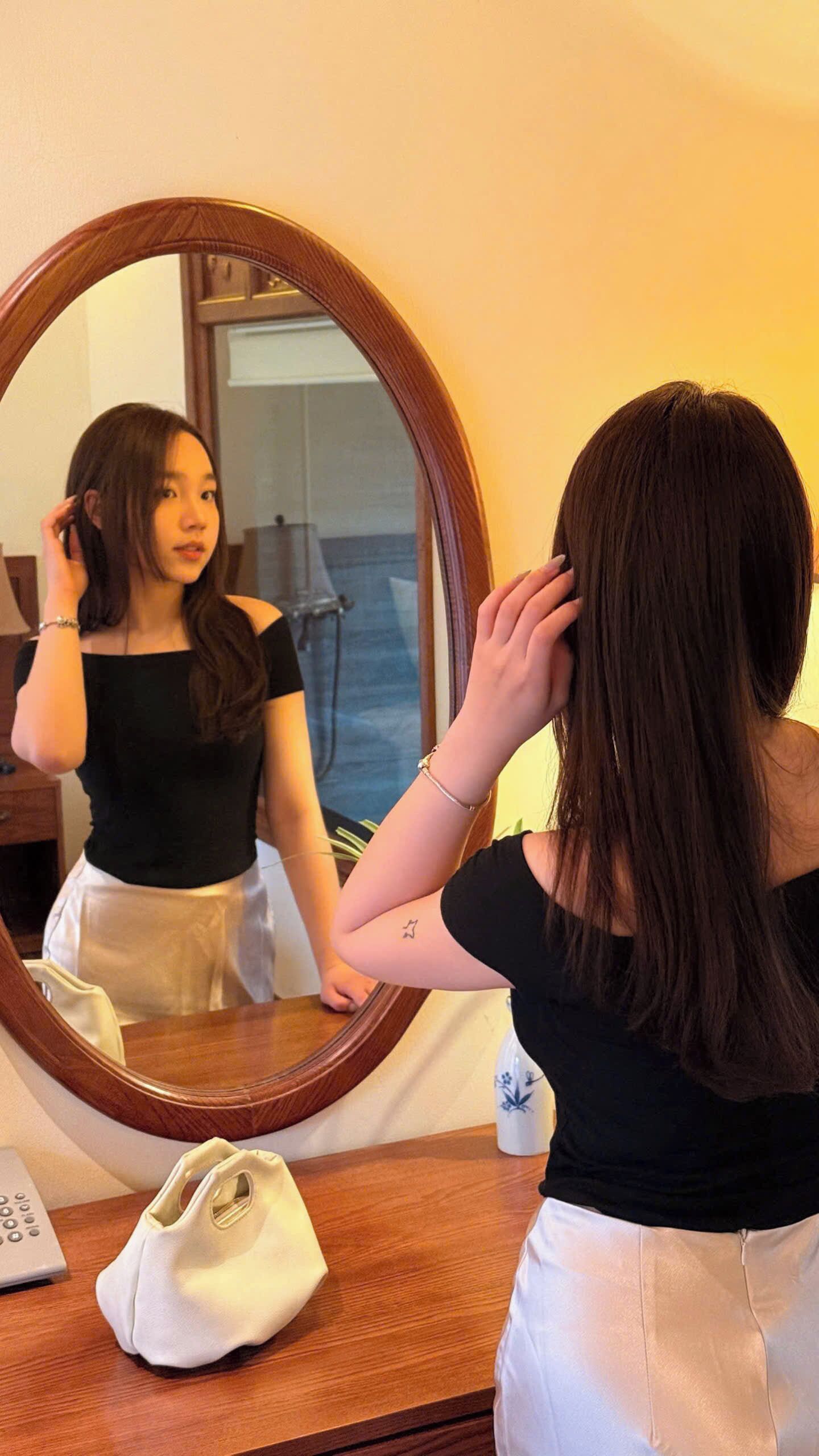 A person standing in front of a mirror with a wooden frame, adjusting their hair.