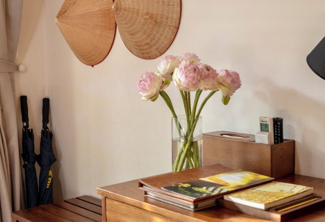 A wooden desk with a vase of flowers, a book, and a tissue box.