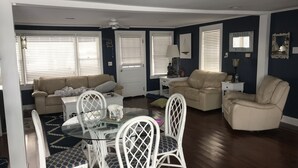 A living room with a beige sofa, a white armchair, a glass-top coffee table, and a white dining set.