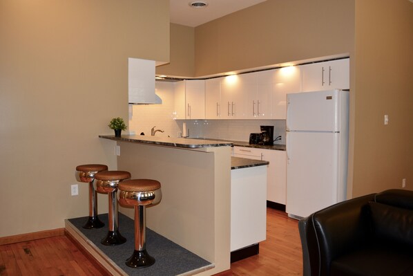 A compact kitchen with white cabinets, a built-in island with stools, a refrigerator, and a coffee maker.
