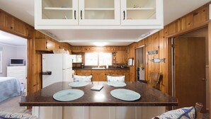 Une cuisine avec des meubles de rangement en bois, un îlot central doté de sets de table et une fenêtre au-dessus de l’évier.
