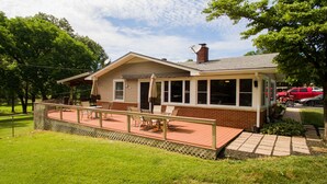 Une maison à deux étages dotée d’un patio couvert, d’une cheminée en briques et d’une antenne parabolique.