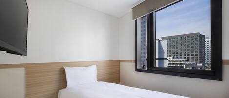 Una habitación de hotel con una cama individual, un ventanal con vistas a la ciudad y un televisor de pantalla plana sujeto a la pared.
