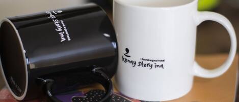 Una taza blanco y negro con texto, una tetera verde y un teclado sobre una mesa.