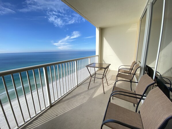 A balcony with a glass table and chairs, overlooking a beach and the ocean. - Beautiful Beachfront Majestic Beach Resort, T1-1605, Great Amenities, CLEAN (Panama City Beach)