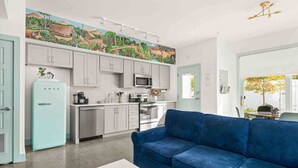 A modern kitchen with white cabinets, a blue refrigerator, and a mural on the wall.