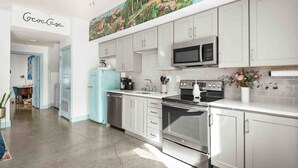 A modern kitchen with white cabinets, stainless steel appliances, and a colorful mural on the wall.