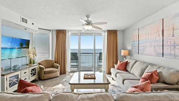 A spacious living room with a large TV, comfortable seating, a ceiling fan, and a balcony with a view of the ocean. - Beach Themed Oceanfront Condo, Outdoor Hot Tubs | Crescent Shores - N 805 (North Myrtle Beach)