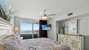 A bedroom with a bed, a ceiling fan, a television, a dresser, and a view of the ocean. - Beach Themed Oceanfront Condo, Outdoor Hot Tubs | Crescent Shores - N 805 (North Myrtle Beach)