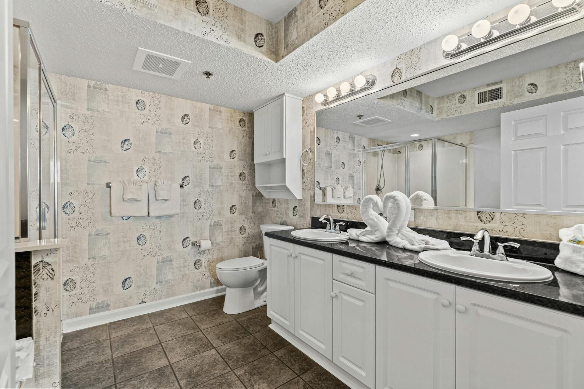 Une salle de bain avec un grand miroir, deux lavabos, des toilettes et une douche.
