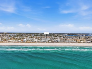 A coastal property with a beach view, a sign indicating 'PROPERTY', and a dense residential area in the background.
