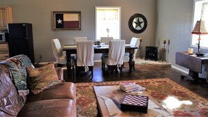 Un salon avec un canapé en cuir, une table basse avec des livres, une table à manger avec des chaises, un drapeau accroché au mur et une décoration en forme d’étoile.