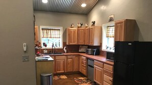Une cuisine avec des meubles de rangement en bois, un réfrigérateur noir et une fenêtre avec des rideaux.