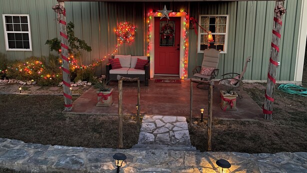 Un bâtiment rustique avec une porte rouge, une véranda dotée de sièges extérieurs et des décorations festives.