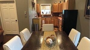 Un coin repas avec une table en bois, des chaises blanches et un bol rempli de biscuits.