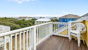 A wooden deck with a white railing, a blue house in the background, and a view of the ocean. - Large, Pet Friendly, Private Pool, Golf Cart,Easy Beach Access (Emerald Isle)