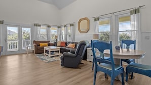 A spacious living room with a sofa, armchairs, a coffee table, and a dining table with chairs. There are large windows with curtains, a ceiling fan, and a mirror on the wall. - Large, Pet Friendly, Private Pool, Golf Cart,Easy Beach Access (Emerald Isle)