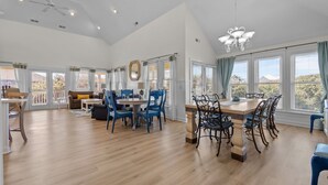 A spacious living area with a dining table, blue chairs, and a chandelier. - Large, Pet Friendly, Private Pool, Golf Cart,Easy Beach Access (Emerald Isle)