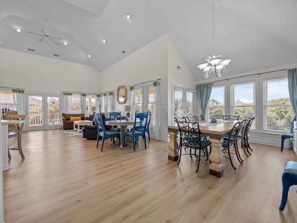 A spacious living area with a dining table, blue chairs, and a chandelier.
