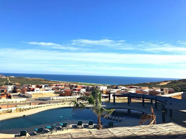 Un resort con piscina, sillas de descanso y vistas al océano y las colinas.