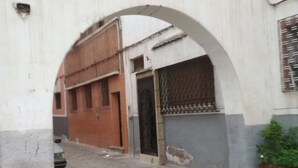 Een smalle straat met cobblestones, met een grote boog die leidt naar een gebouw met een metalen poort.
