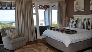 Ein Schlafzimmer mit einem großen Bett, einem Sessel, Blick durch eine Schiebetür und Kunstwerken an der Wand.