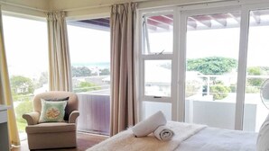 Ein Schlafzimmer mit Bett, Stuhl, großem Fenster und Blick ins Freie.