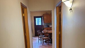 A hallway with wooden flooring leading to a dining area with a table and chairs. - Bishop Lake Three Bedroom Cabin  (Crandon)