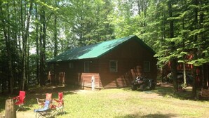 A log cabin with a green roof, surrounded by a grassy yard and trees. - Bishop Lake Three Bedroom Cabin  (Crandon)