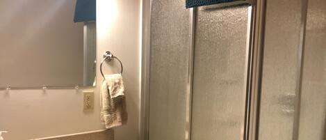 Un baño con tocador de madera, lavabo, espejo y ducha con mampara de vidrio.
