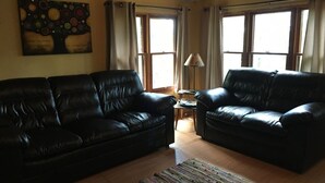 A living room with two black leather sofas, a wooden floor, a colorful rug, a lamp, and a painting on the wall. - Bishop Lake Three Bedroom Cabin  (Crandon)