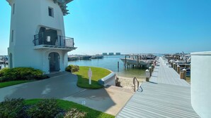 Une tour blanche dotée d’un balcon, un port de plaisance avec des bateaux et un ciel bleu azur.