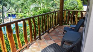 A balcony with two wicker chairs and a small table, overlooking a swimming pool and lush greenery. - Fresh & bright suite, private kitchen, amazing garden view, walk to beach, yoga (Puerto Escondido)