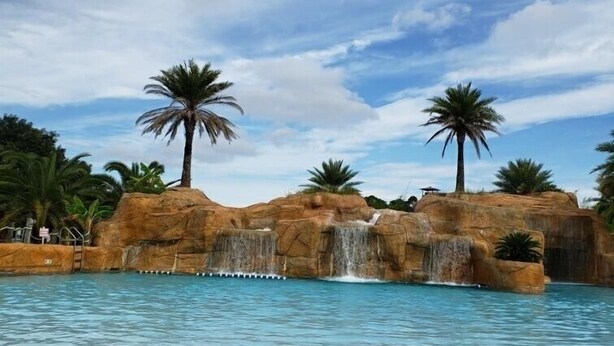 A pool with a waterfall feature, palm trees, and a beach chair.