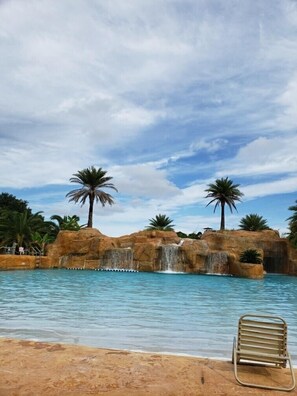 A pool with a waterfall feature, palm trees, and a beach chair.