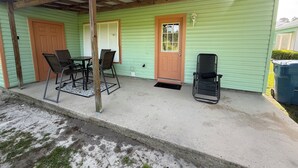 A covered porch with a table and chairs, a single door, and a trash bin.