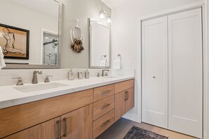 Un baño moderno con un espejo grande, dos lavamanos, armarios de madera y una puerta blanca.